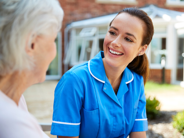 Senior woman sitting on a bench, talking with nurse in a retirement home